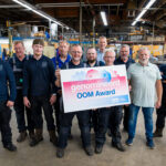 Medewerkers van RVS Noord in de werkplaats met een bord voor hun nominatie voor de OOM Award.